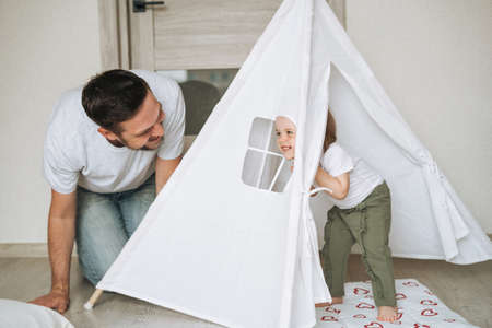 Happy father young man feeds baby girl little daughter in kitchen at homeの写真素材