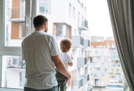 Happy father young man feeds baby girl little daughter in kitchen at homeの写真素材