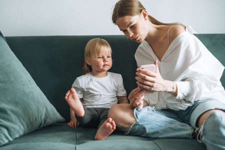 Young mother and cute baby girl using mobile phone at homeの写真素材