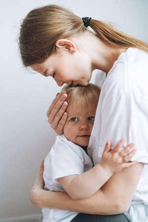 Vertical portrait of young woman mother kissing baby girl daughter on hands at home