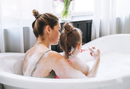 Young mother woman with long hair with little tween girl daughter in pajamas washing face and hands...