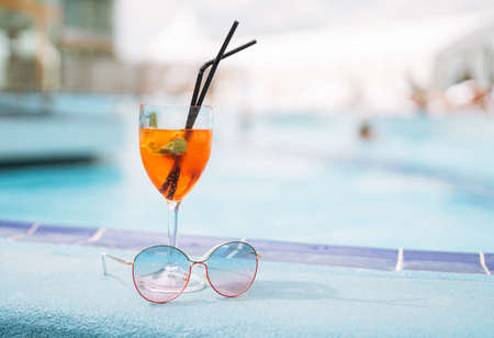 Glass of cocktail with ice and sunglasses on hotel pool, summer vacationの写真素材
