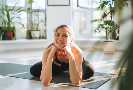 Young fit woman practice yoga doing asana namaste in light yoga studio with green house plant