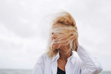 Portrait of Elegant blonde woman in white shirt on sand beach at storm seaの写真素材