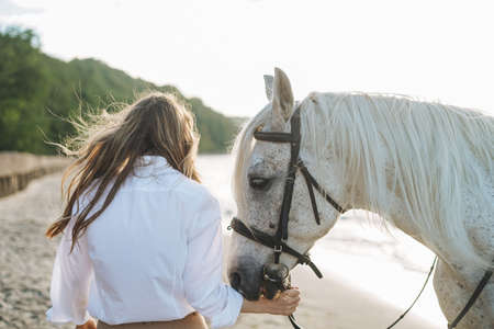 Young long hair woman in white shirt riding white horse on seascape backgroundの写真素材