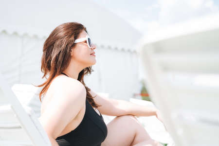 Stylish happy young woman plus size body positive in black swimsuit and sunglasses near hotel spa pool, summer vacationsの写真素材
