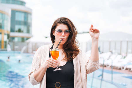 Stylish happy young woman plus size body positive in black swimsuit and sunglasses near hotel spa pool, summer vacationsの写真素材