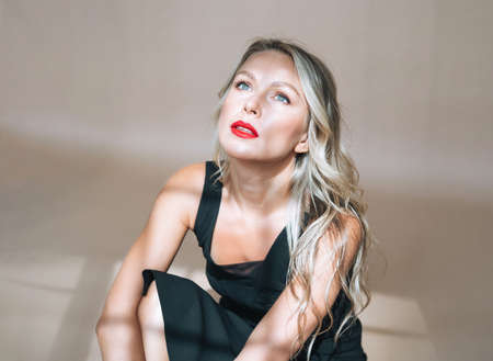 Portrait of gorgeous happy blonde young woman with bright makeup in evening dress on beige backgroundの写真素材