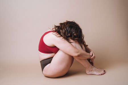 Self loving young woman plus size in sport wear doing exercises with dumbbells on beige background, body loveの写真素材