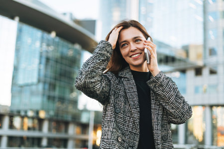 Young smiling woman in coat taling selfie on mobile phone in evening city streetの写真素材