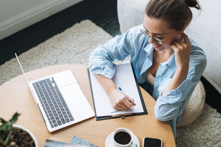 Smiling woman with long hair in beige cardigan drinking coffee and using mobile phone at home