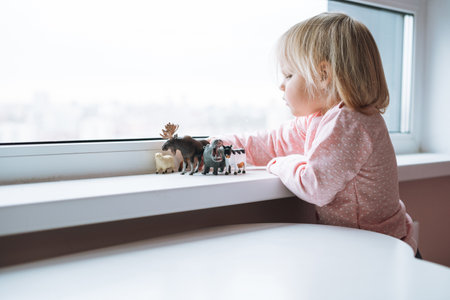 Little girl toddler playing with animal toys on table in children's room at homeの写真素材