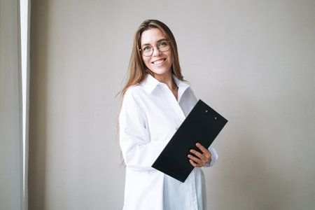 Portrait of young smiling brunette woman with documents in hands on background of gray wallの写真素材