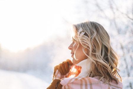 Portrait of smiling blonde woman in winter clothes in snowy winter forest in golden hourの写真素材