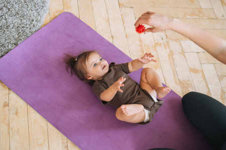 Young woman fit mom with baby girl doing exercises with massage ball on mat at the homeの写真素材