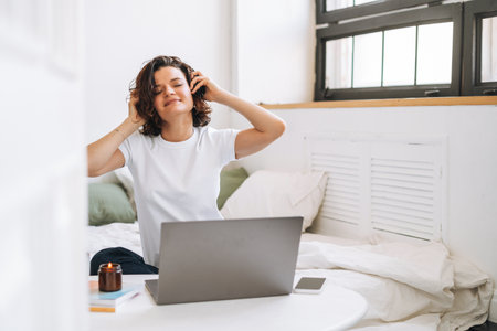 Young brunette woman with closed eyes in headphones working on laptop from homeの写真素材