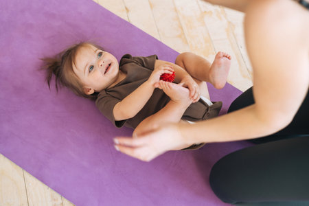 Young woman fit mom with baby girl doing exercises with massage ball on mat at the homeの写真素材