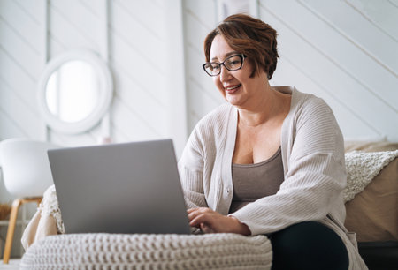 Smiling middle aged plus size woman working on laptop from homeの写真素材