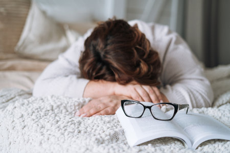 Sleeping middle aged woman withbook lying on bed at homeの写真素材
