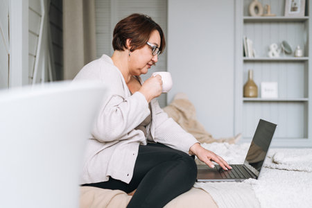 Smiling middle aged plus size woman working on laptop from homeの写真素材