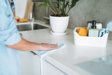 Box with things for cleaning kitchen on background of young woman at homeの写真素材
