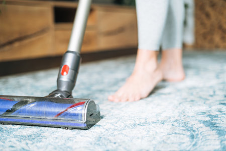 Close up photo of young woman using vacuum cleaner cleaning carpet floor at homeの写真素材