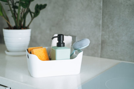 Kitchen cleaning supplies brush, liquid soap, dish sponge in container on kitchen counter at homeの写真素材