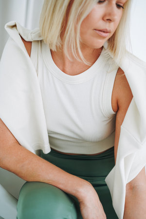 Close up portrait of young blonde woman in sportswear sitting on background of white wallの写真素材