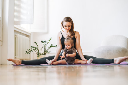 Young woman fit mom with baby girl doing fitness on mat at homeの写真素材