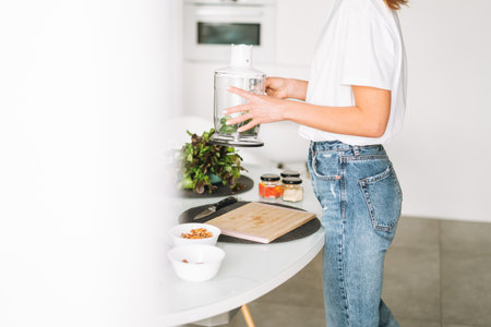 Young slim woman in white t-shirt and blue jeans cooking smoothie healthy food in kitchen at home