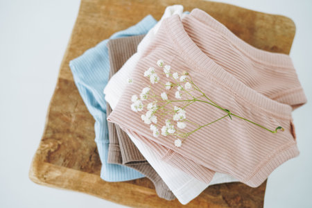 Stack of cotton tops in natural tones on wooden chair in bright room, view from topの写真素材