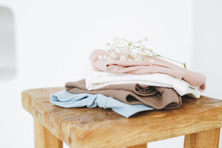 Stack of cotton tops in natural tones on wooden chair in bright roomの写真素材