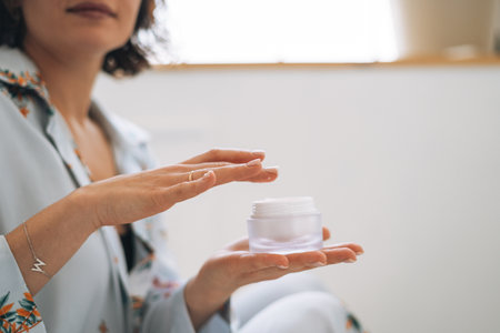 Young woman in cozy blue pajamas using cosmetic cream in hands at homeの写真素材