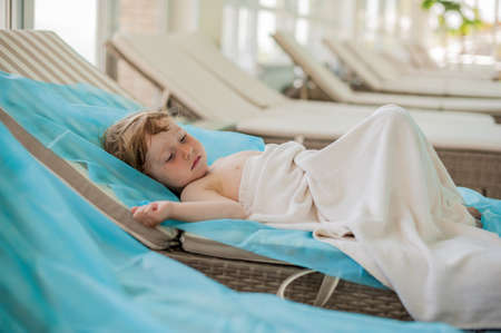 The boy is resting on a sun lounger by the poolの写真素材
