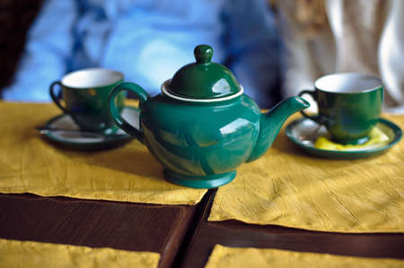 Green teapot and two cups of tea on the yellow tableclothの写真素材