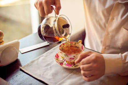 A man pours the tea into a cup with flowersの写真素材