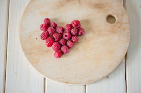 Raspberries in a heart on a wooden board