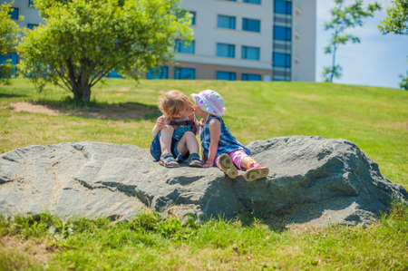 Toddlers Boy and girl kissing in summer park on a large rockの写真素材