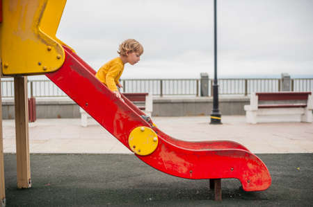 Toddler boy on children's slide on playground, by the sea