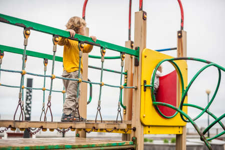 Active little child playing on climbing net and jumping on trampoline at school yard playground. Kids play and climb outdoors on sunny summer day. Funny boy on nest swing at preschool sport center.の写真素材