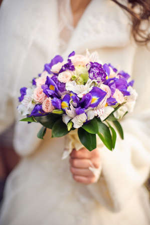 Bride holding white and purple wedding bouquet against gownの写真素材