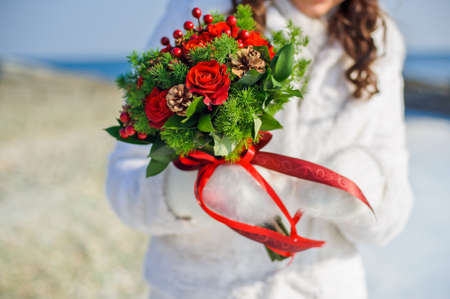 Bride holding a bouquet of red roses and pine cones in snowの写真素材