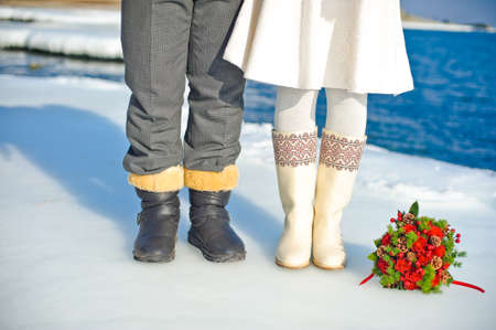 Bouquet of roses and fir cones on the ice and legs of bride and groomの写真素材