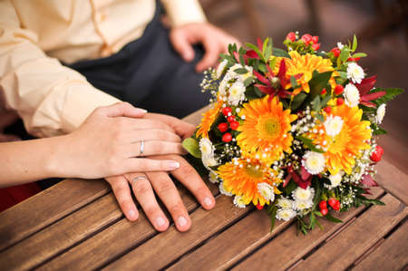 Orange gerberas bouquet on a wooden table, hands of a bride and groom