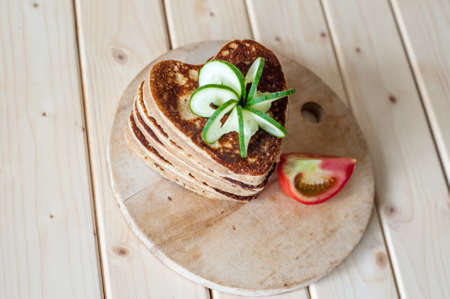 Pancake hearts on a wooden background and carving a cucumberの写真素材