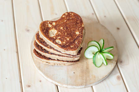 Pancake hearts on a wooden background and carving a cucumberの写真素材