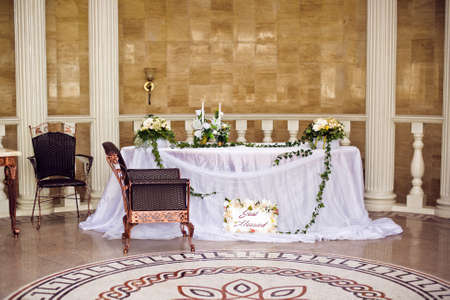 Beautiful flower composition outdoors. Wedding floristic decoration at wooden table, bouquet of colorful wildflowers and white roses in glass vase at green leaves backgroundの写真素材
