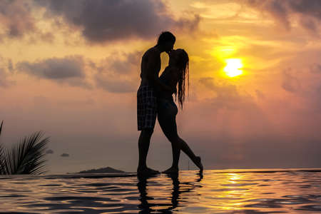 Silhouette of a woman and men on the panoramic swimming pool at sunset backgroundの写真素材