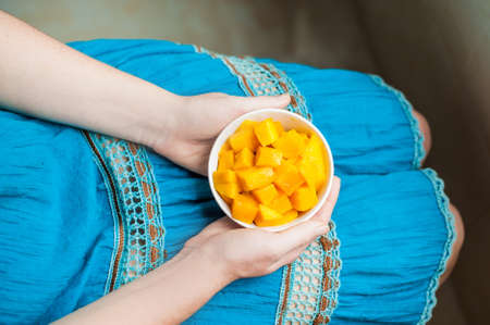 Bowl of healthy fresh mango in the hands of a young woman in a blue dressの写真素材