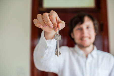 Men's hands hold house key on a background of a wooden door. Owning real estate concept.の写真素材